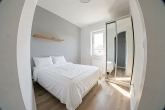Petite chambre de moins de 9m2 bien aménagée avec lit simple, étagère flottante et armoire à portes miroir dans un studio compact