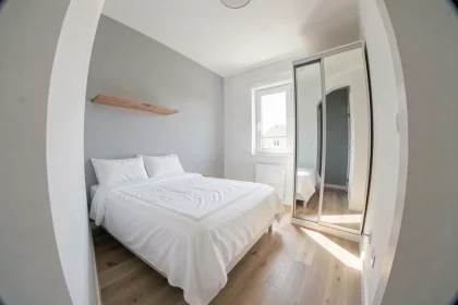 Petite chambre de moins de 9m2 bien aménagée avec lit simple, étagère flottante et armoire à portes miroir dans un studio compact